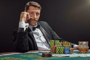 hermoso emocional hombre es jugando póker sentado a el mesa en casino en contra un blanco destacar. foto