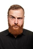 Portrait of a young, chubby, redheaded man in a black shirt making faces at the camera, isolated on a white background photo