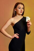 Blonde woman with bright make-up, in black dress is showing two aces, posing against colorful background. Gambling, poker, casino. Close-up. photo