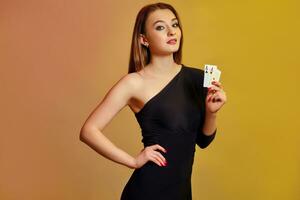 Blonde lady with bright make-up, in black dress is showing two aces, posing against colorful background. Gambling, poker, casino. Close-up. photo