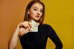 Blonde female with bright make-up, in black dress is showing two aces, posing against colorful background. Gambling, poker, casino. Close-up. photo