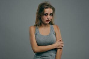 Blonde girl with bruises on her face posing against gray studio background. Domestic violence, abuse. Depression, despair. Close-up, copy space. photo