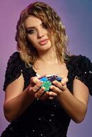 Blonde lady in black sequin dress is holding handful of multicolored chips, posing on colorful studio background. Gambling, poker, casino. Close-up. photo