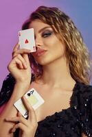 Brown-haired maiden with curly hair, in black dress holding two aces near her face, posing on colorful background. Gambling, poker, casino. Close-up. photo