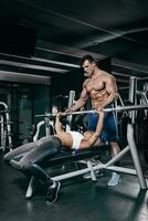 Personal trainer helping a young woman lift a barbell while working out in a gym photo