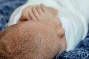 Newborn - baby, face close-up. The sleeping Newborn boy under a white knitted blanket lies on the blue fur. photo