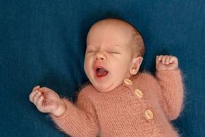 Newborn baby boy 14 days wearing knitted suit sleeping in bed close-up. photo