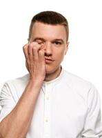 Charming handsome young man in a white shirt is making faces, while standing isolated on a white background photo