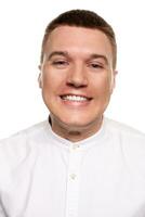 Charming handsome young man in a white shirt is making faces, while standing isolated on a white background photo