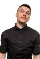 Handsome young man in a black shirt is making faces, while standing isolated on a white background photo