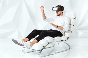 Excited young man is getting experience using VR-headset glasses of virtual reality gesticulating with his hands photo