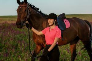 hermosa joven niña sonrisa a su caballo vendaje uniforme competencia al aire libre retrato en puesta de sol foto