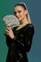 Blonde female in jewelry and black sequin dress. Smiling, showing some hundred dollar bills, posing on colorful background. Poker, casino. Close-up photo