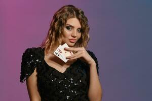 Brown-haired maiden with curly hair, in black dress showing two aces, posing on colorful background. Gambling entertainment, poker, casino. Close-up. photo