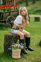 Dreamy preteen girl sitting on stump in green summer park with basket of wildflowers nearby photo