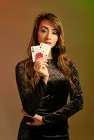 Brunette female in black dress showing two red chips and aces, posing against colorful studio background. Gambling, poker, casino. Close-up. photo