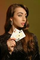 Brunette maiden in black velvet dress and jewelry showing two aces, posing against colorful studio background. Gambling, poker, casino. Close-up. photo