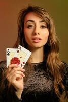 Brunette lady in black dress showing two red chips and aces, posing against colorful studio background. Gambling, poker, casino. Close-up. photo