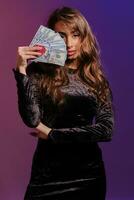 Brunette girl in black velvet dress showing two red chips and some cash, posing against coloful background. Gambling, poker, casino. Close-up. photo