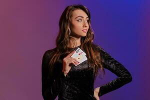 Brunette woman in black velvet dress showing two playing cards, posing against coloful background. Gambling entertainment, poker, casino. Close-up. photo