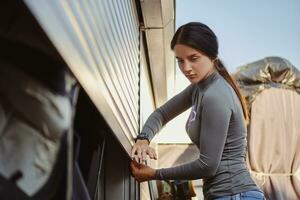 Beautiful brunette female in gray turtleneck and blue denim shorts is closing her wakeboard and equipment storage garage. Close-up. photo