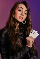 Brunette woman in black velvet dress showing two playing cards, posing against coloful background. Gambling entertainment, poker, casino. Close-up. photo