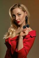 Blonde lady with bright make-up, in red dress and black earrings. She showing two chips, posing on colorful background. Poker, casino. Close-up photo