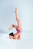 Flexible girl gymnast in beige leotard is performing complex elements of gymnastics while posing isolated on white background. Close-up. photo