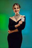 Brunette lady in black dress, shiny necklace and earrings. She is smiling, showing two aces, posing on colorful background. Poker, casino. Close-up photo