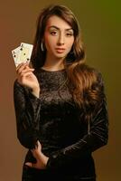 Brunette woman in black velvet dress and jewelry showing two aces, posing against colorful studio background. Gambling, poker, casino. Close-up. photo