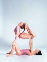 Two flexible girls gymnasts in beige leotards performing complex elements of gymnastics using support, posing isolated on white background. Close-up. photo