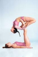 Two flexible girls gymnasts in pink leotards are doing exercises using support and posing isolated on white background. Close-up. photo