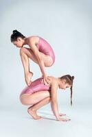 Two flexible girls gymnasts in beige leotards performing complex elements of gymnastics using support, posing isolated on white background. Close-up. photo