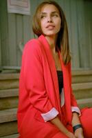 Blonde girl in red lady-type pantsuit and black top, watch, ring, pendant around her neck is posing sitting on a stairs. Fashion and style. Close-up. photo