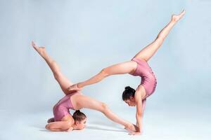 dos flexible muchachas gimnastas en rosado leotardos son haciendo ejercicios utilizando apoyo y posando aislado en blanco antecedentes. de cerca. foto