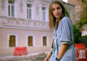 rubia niña en largo azul vestir y un pequeño negro bolso en su hombro es posando cerca un rojo Barandilla, caminando solo en el ciudad. de cerca disparo. foto