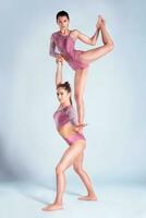 Two flexible girls gymnasts in beige leotards performing complex elements of gymnastics using support, posing isolated on white background. Close-up. photo