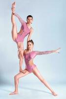 Two flexible girls gymnasts in beige leotards performing complex elements of gymnastics using support, posing isolated on white background. Close-up. photo