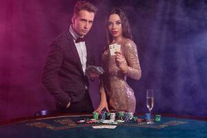 hombre y mujer jugando póker a casino, celebrando ganar a mesa con pilas de papas fritas, dinero, tarjetas, champán. negro, fumar antecedentes. de cerca. foto
