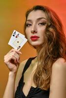 Brunette woman with earring in nose, in black dress. Showing two aces, posing on colorful background. Gambling, poker, casino. Close-up photo