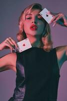 Blonde girl in black stylish dress showing two playing cards, posing against colorful background. Gambling entertainment, poker, casino. Close-up. photo