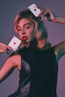 Blonde girl in black stylish dress showing two playing cards, posing against colorful background. Gambling entertainment, poker, casino. Close-up. photo