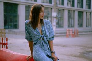 Blonde girl in long blue dress and a small black handbag on her shoulder is posing near a red guardrail, walking alone in the city. Close-up shot. photo