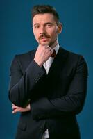 Young business man in classic black suit, white shirt and red bow-tie. Posing against a blue studio background. Mock up, copy space. Close-up. photo