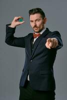 hombre en negro clásico traje y rojo corbata de moño demostración algunos de colores papas fritas, posando en contra gris estudio antecedentes. juego, póker, casino. de cerca. foto