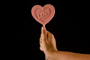 a person holding a pink heart shaped lollipop photo