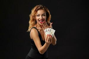 Ginger girl wearing a dark dress is posing holding four aces in her hands standing against a black studio background. Casino, poker. Close-up. photo