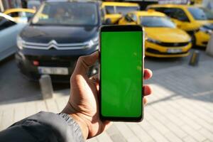 joven hombre mano utilizando inteligente teléfono con verde pantalla con Taxi en antecedentes foto