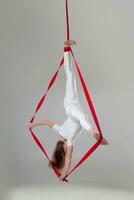 hermosa niña en un blanco deporte traje es ejecutando un acrobático elementos en un estudio. foto