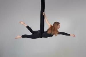 Beautiful girl in a black sport suit is performing an acrobatic elements in a studio. photo